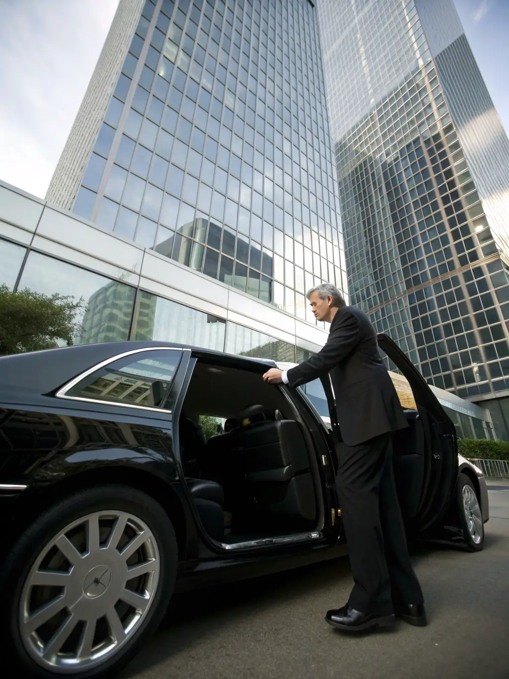 A medium shot of a valet assisting a business professional with their car at an office building, emphasizing the convenience of Valet XO's business valet service.